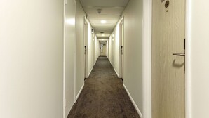 A long, narrow hotel corridor with doors on both sides, a carpeted floor, and a sign indicating room number 026.