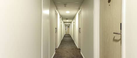A long, narrow hotel corridor with doors on both sides, a carpeted floor, and a sign indicating room number 026.