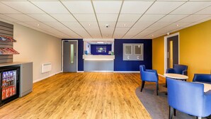 A spacious room with a wooden floor, a reception desk, and blue chairs.