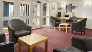 A hotel lobby with a reception desk, a public telephone, and a seating area with chairs and a table.