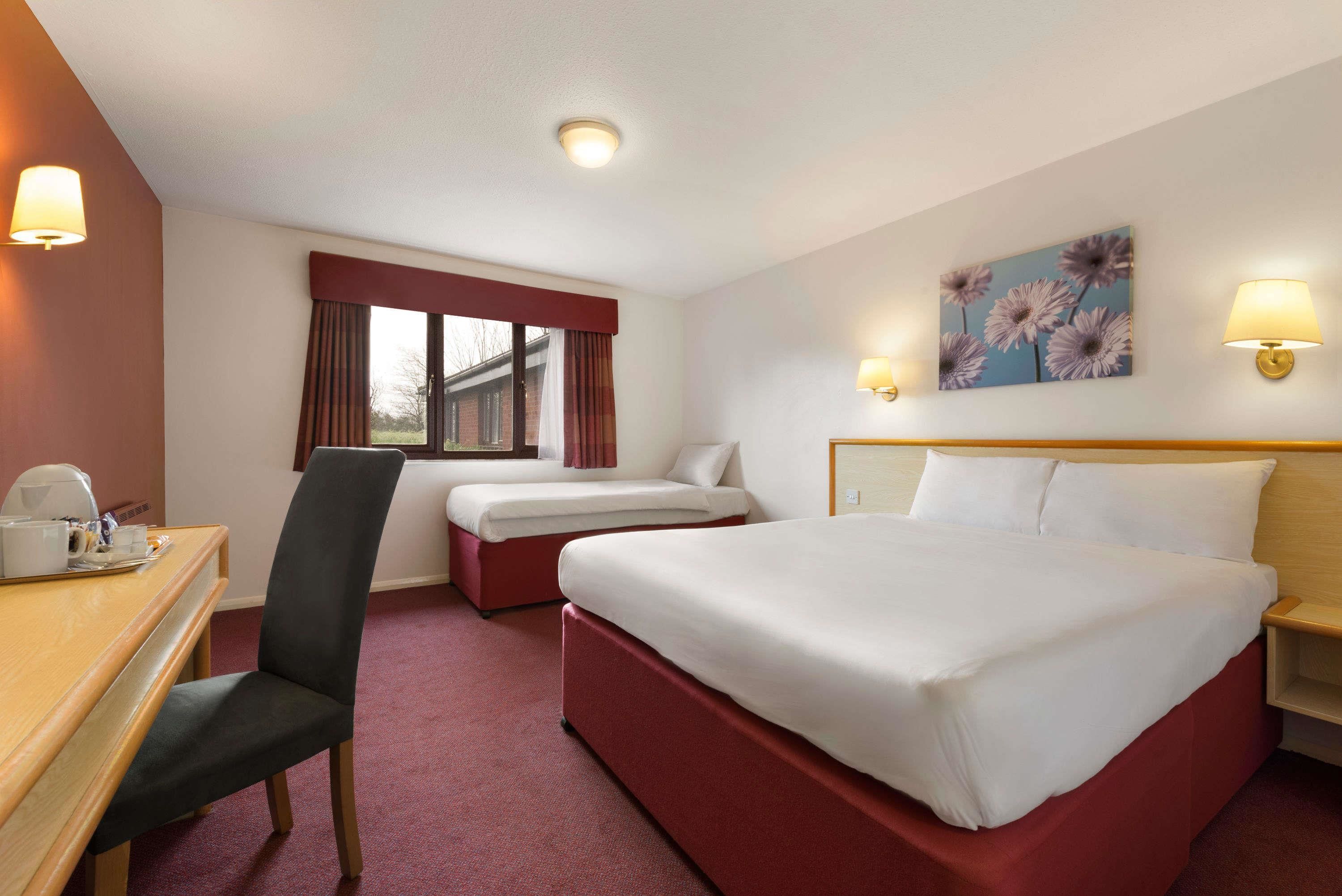 Una habitación de hotel con cama, escritorio, silla y ventana con cortinas.