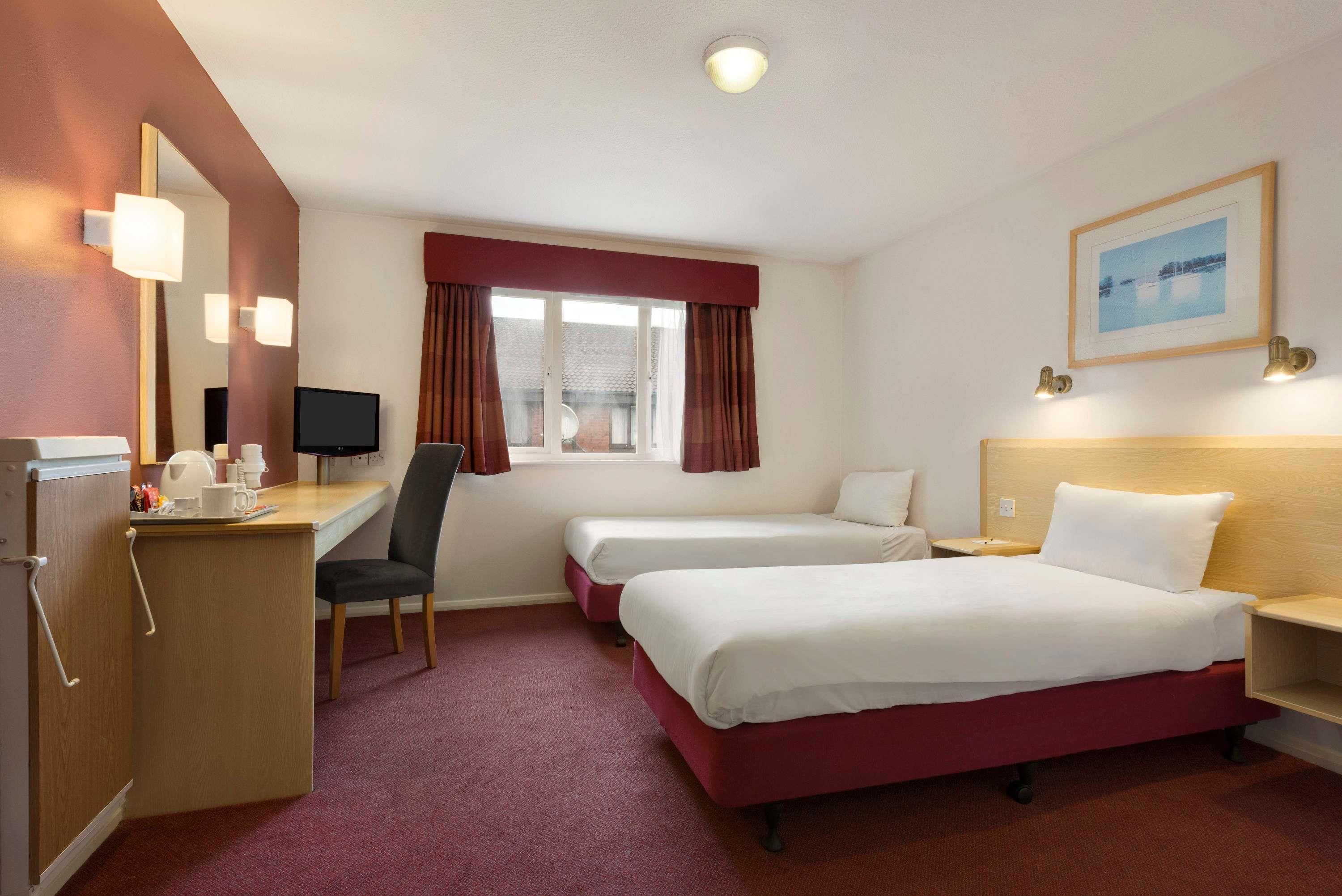 A hotel room with two beds, a desk with a chair, a TV, and a window with curtains.