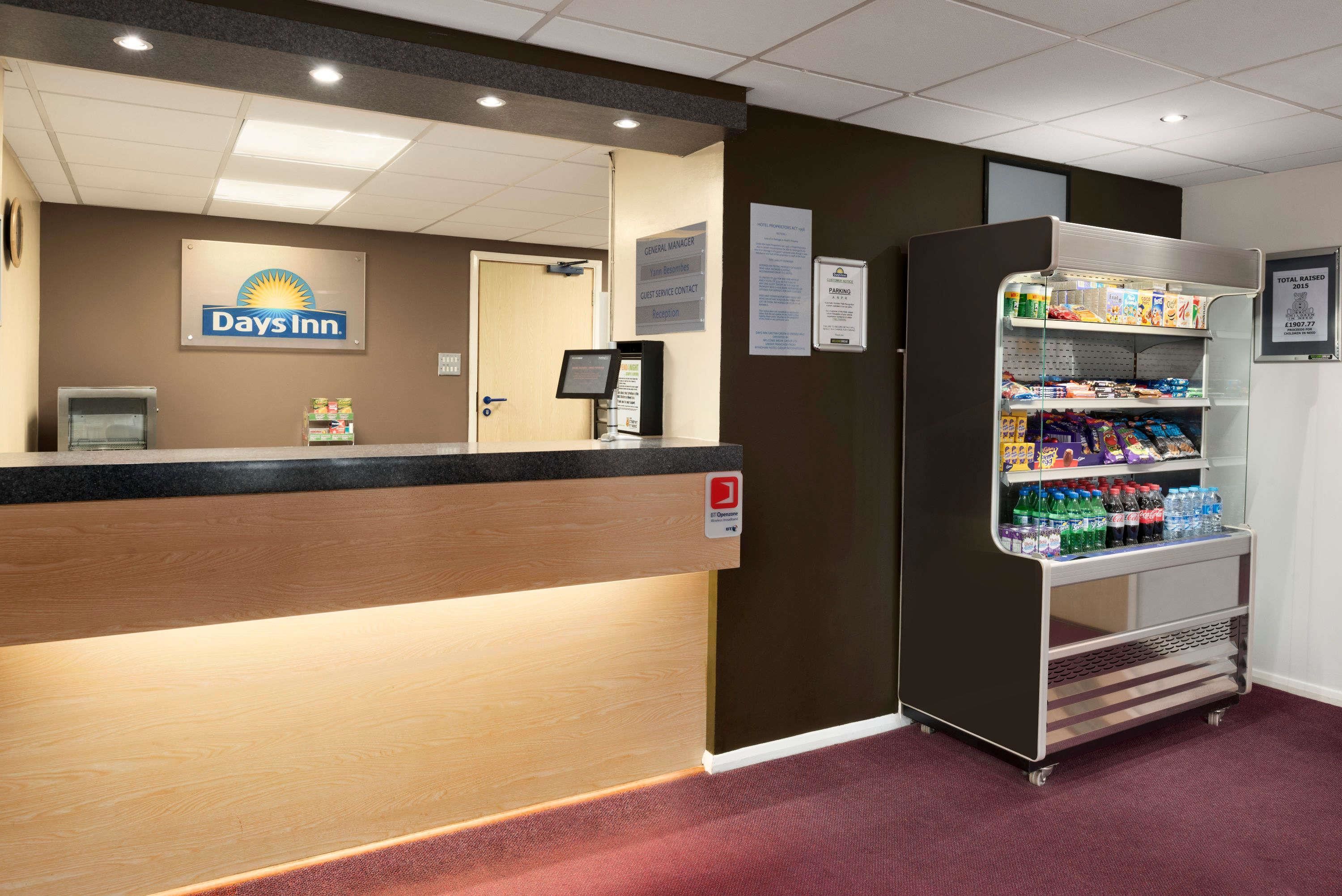 A reception area with a Days Inn sign, a reception desk, a self-service kiosk, and a vending machine with snacks and drinks.