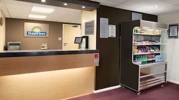 Un'area reception con il cartello Days Inn, una scrivania della reception, un chiosco self-service e una macchina distributrice di snack e bevande.