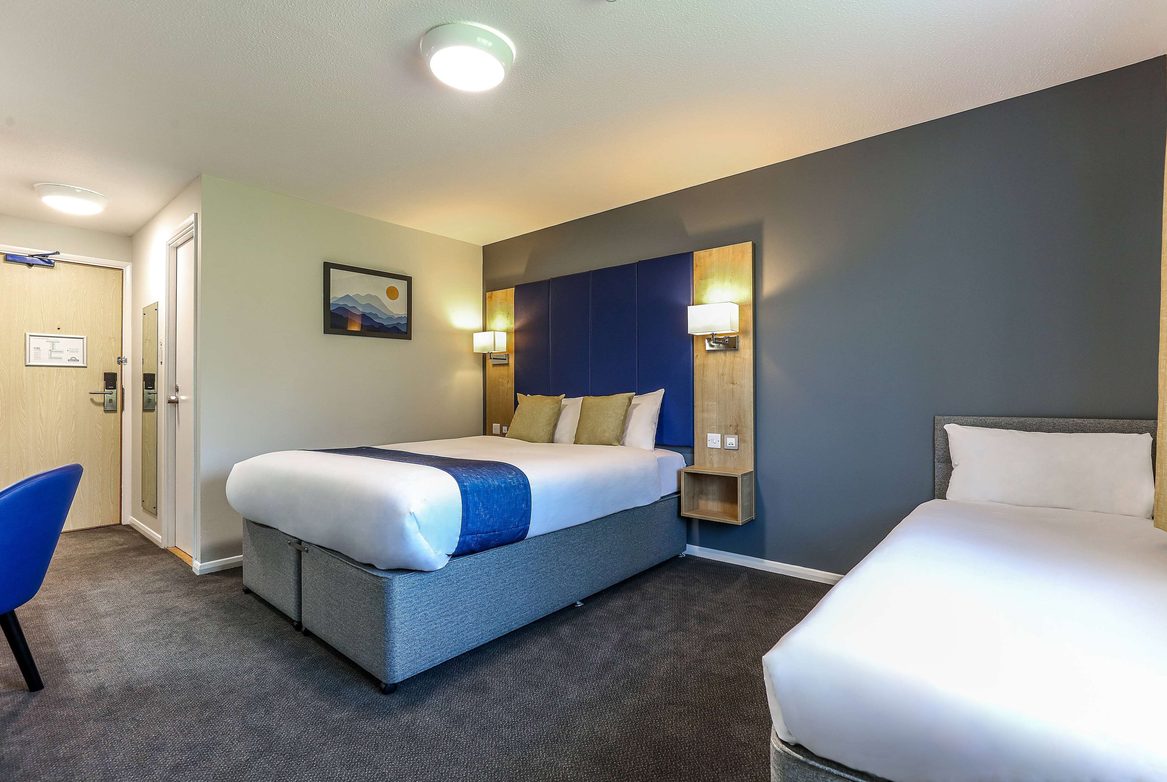 A hotel room with a large bed, a chair, a desk, and a wall-mounted shelf.