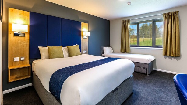 A hotel room with a large bed, two bedside tables, a desk, and a window with curtains.