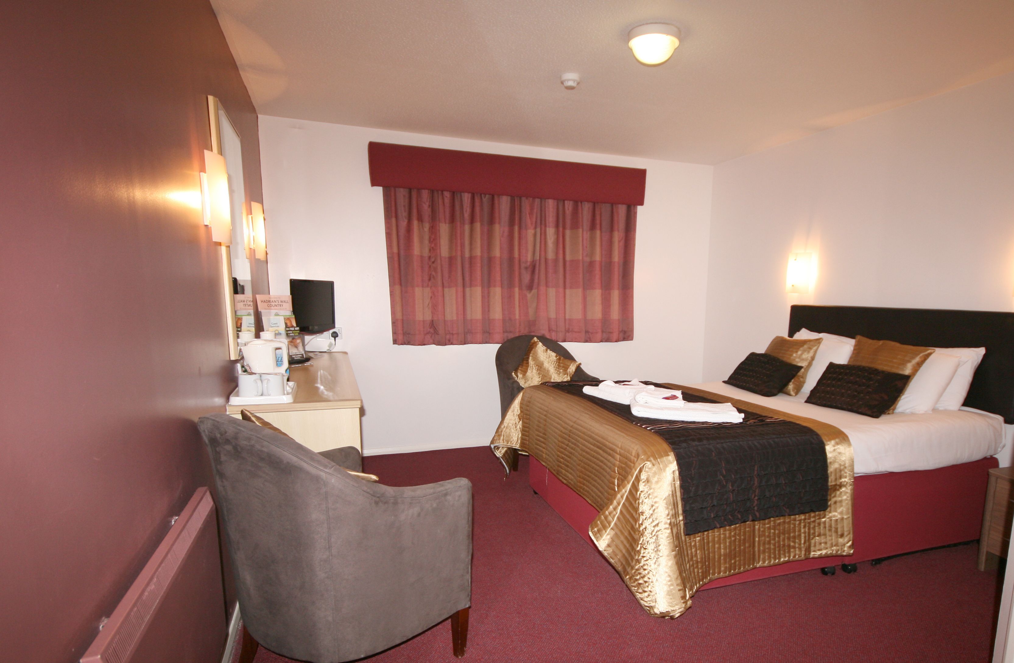 A hotel room with a bed, a desk with a computer, a chair, and a window with curtains.