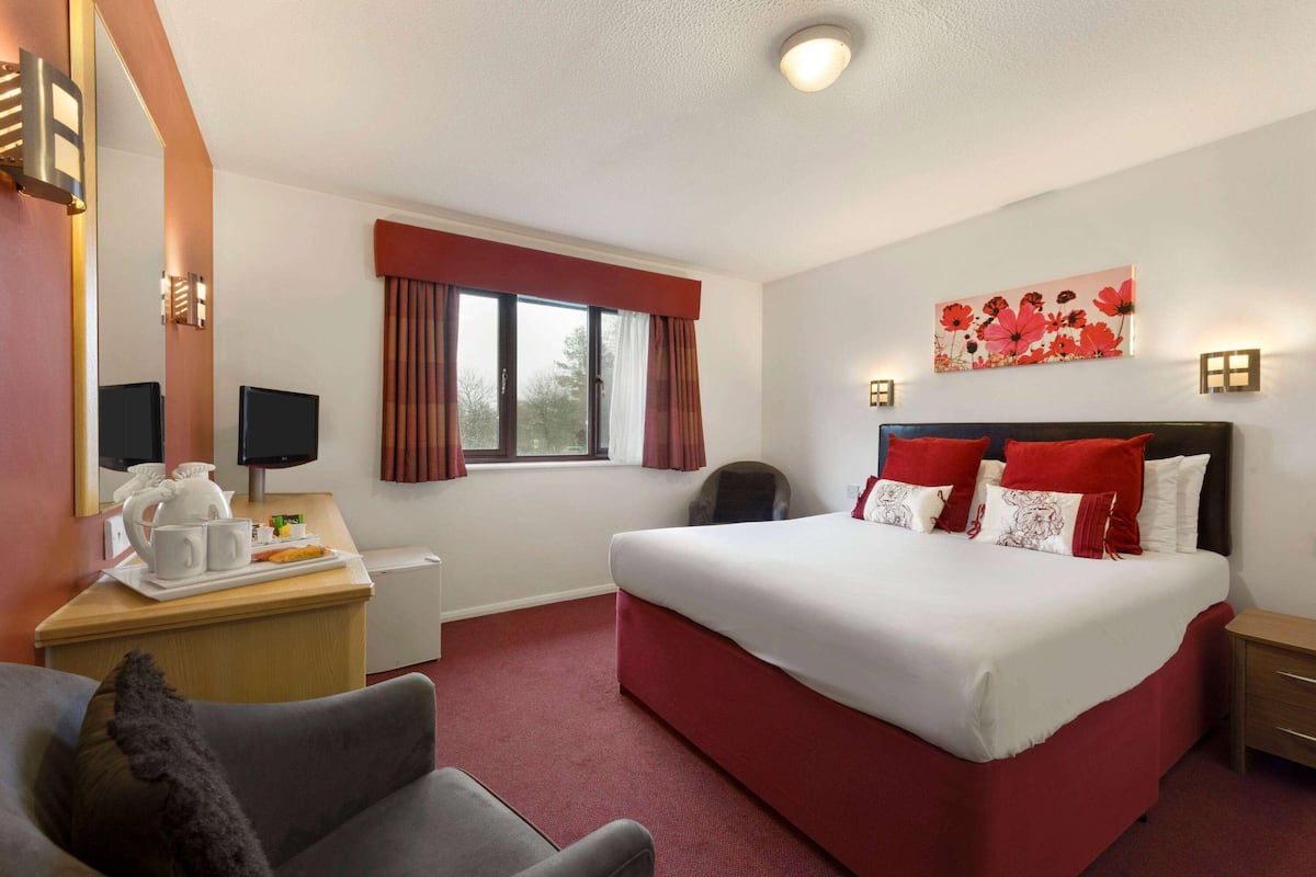 A hotel room with a large bed, a desk with a computer, a chair, and a window with curtains.