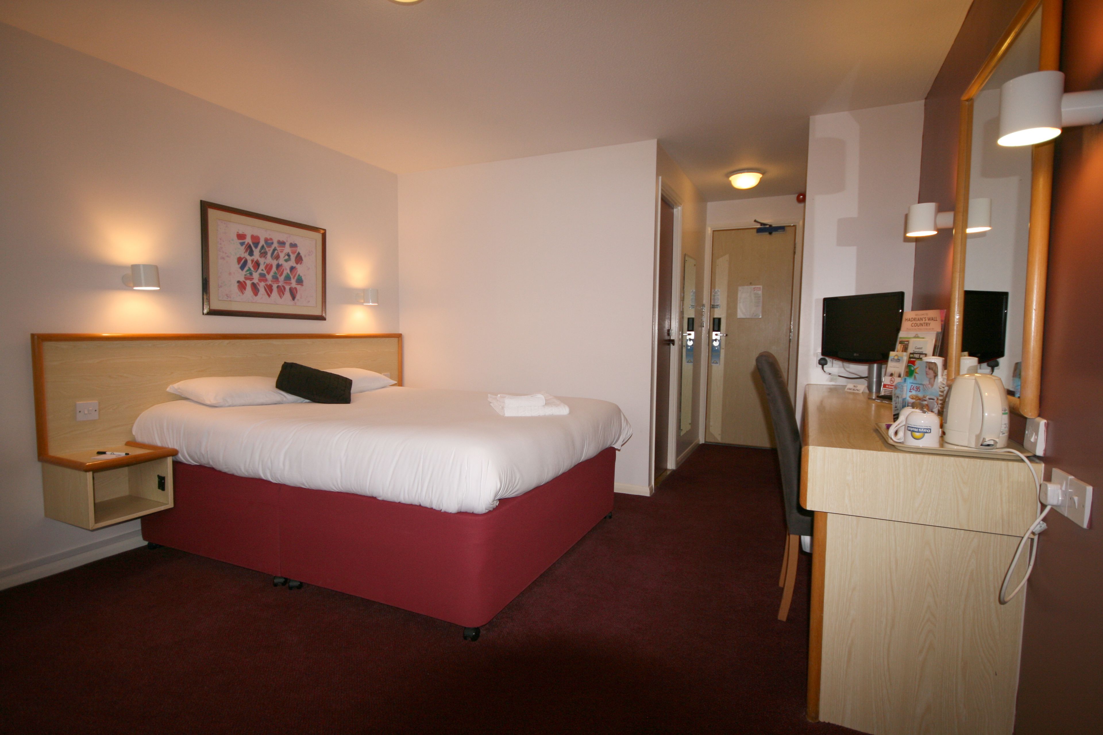 A hotel room with a bed, bedside table, and a desk with a chair.