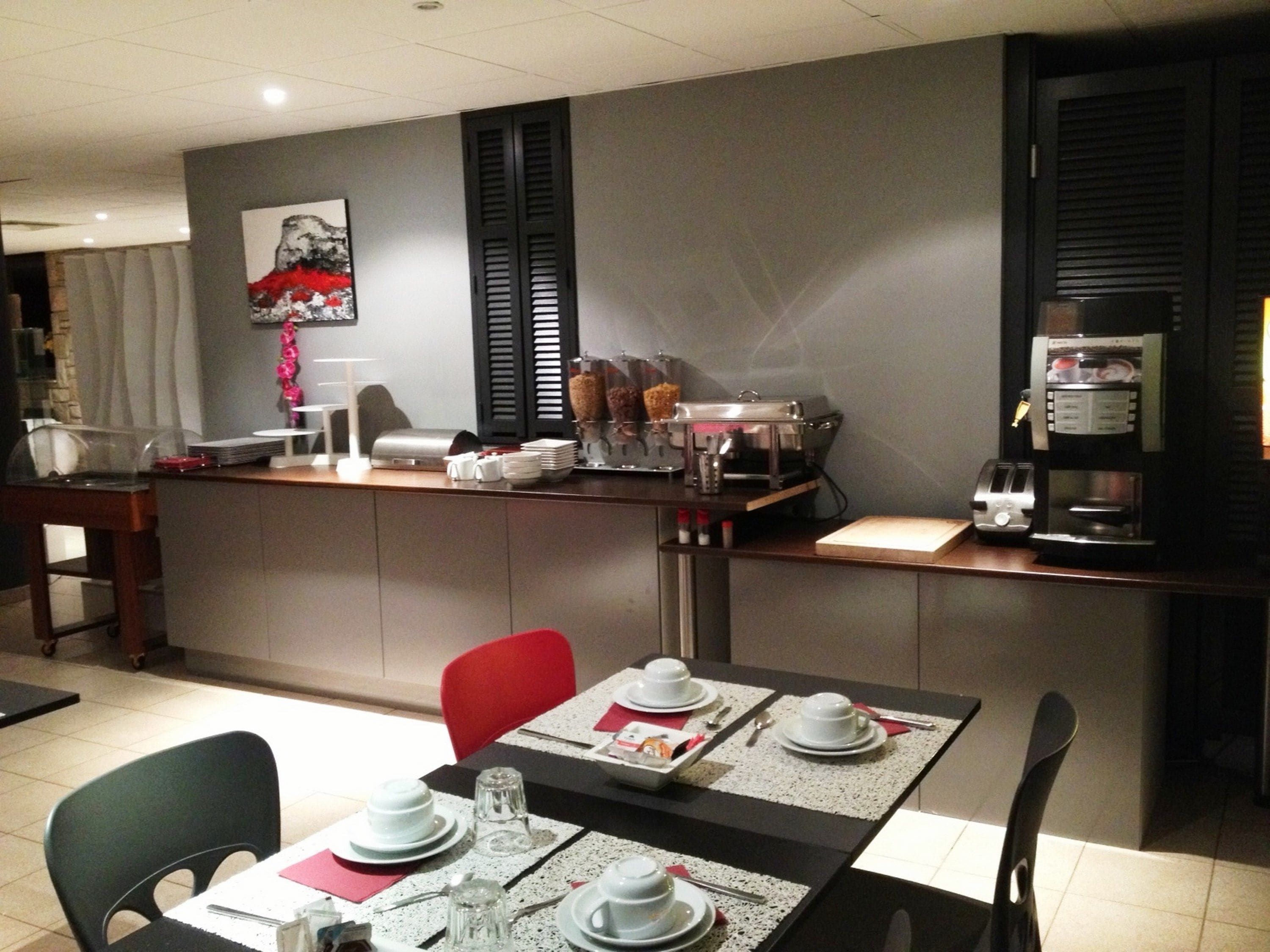 Ett modernt kök med en matplats. Det innehåller en kaffemaskin, ett kylskåp och en arbetsbänk med diverse köksredskap.