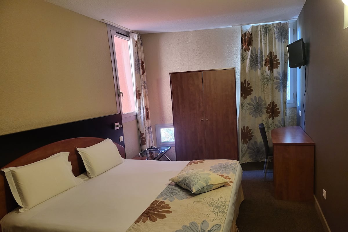 A hotel room with a bed, a desk, a wardrobe, and a TV mounted on the wall.