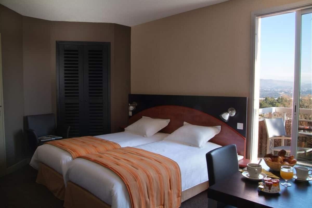 A hotel room with a bed, a desk with breakfast, and a view of the city.