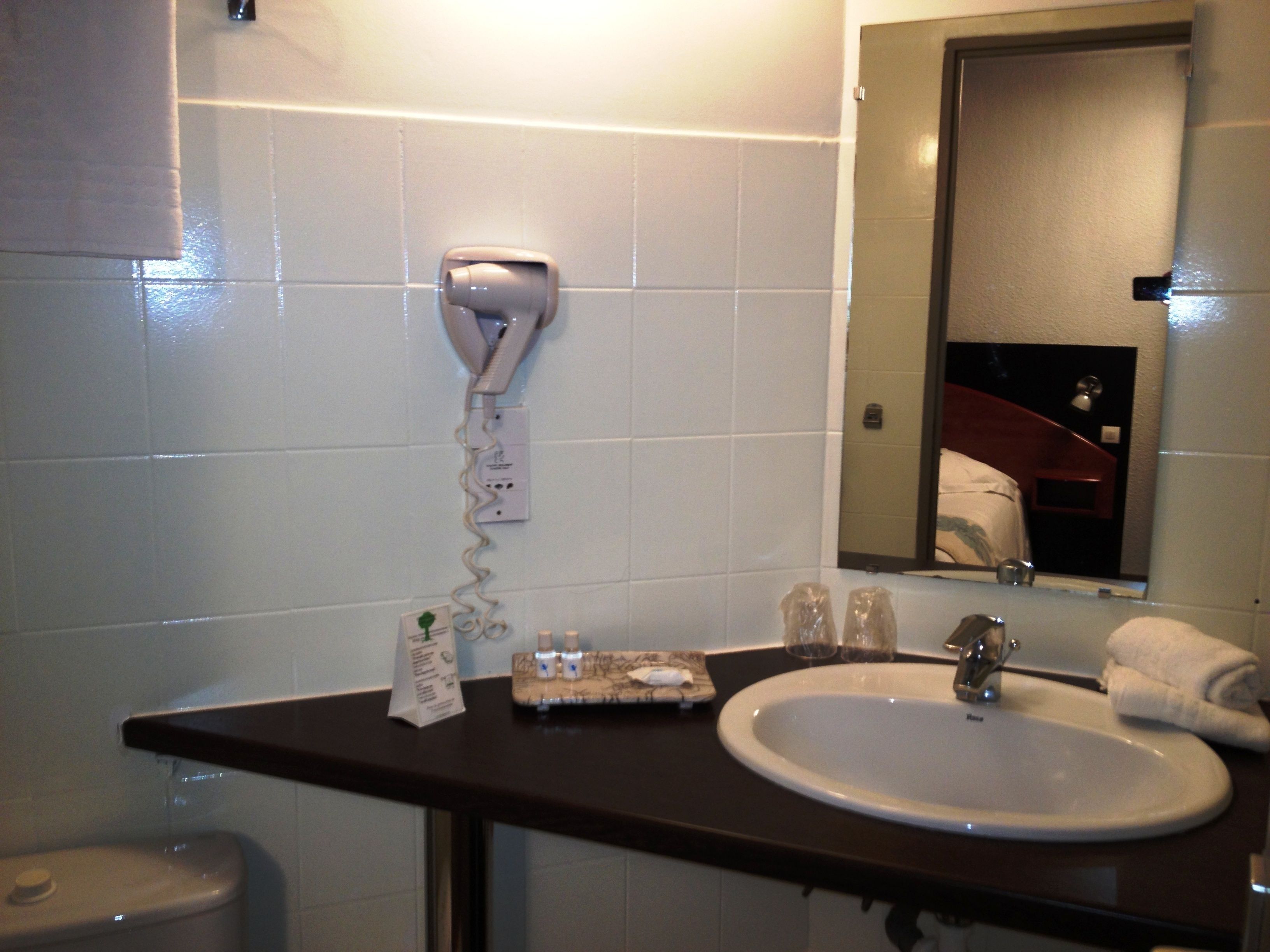 A bathroom with a white sink, a mirror, a towel, and a hairdryer on a wall-mounted outlet.