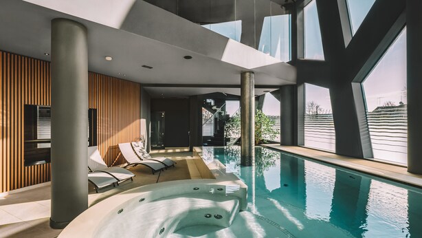 A modern indoor pool area with a hot tub, lounge chairs, and large windows. - Elite Hotel & Spa (Mestre)