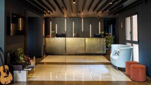 A modern interior with a reception desk, a white sofa, and a guitar on a stand. - Elite Hotel & Spa (Mestre)