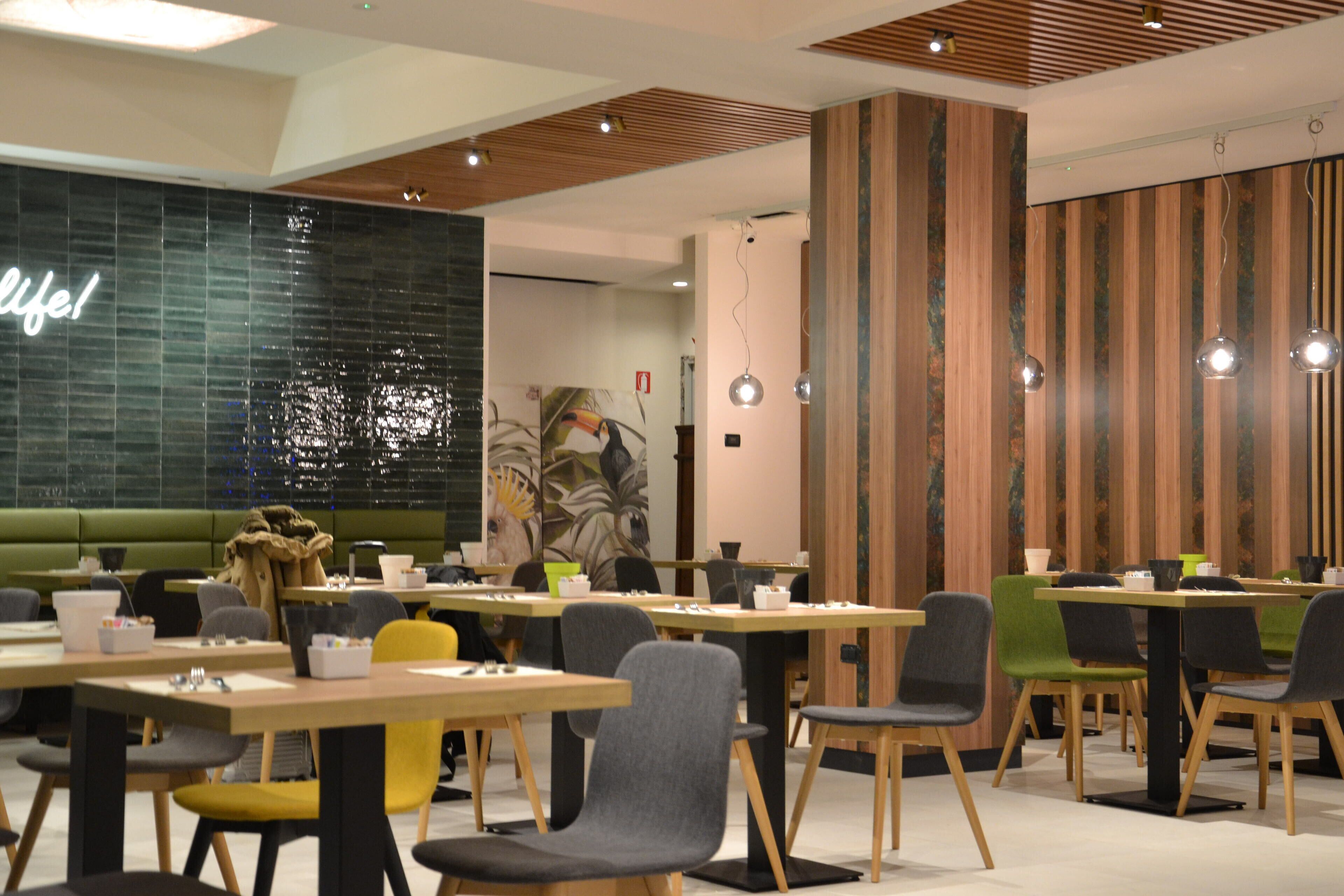 Un espace repas moderne avec des tables et des chaises en bois, un canapé vert et un mur orné d’une inscription « Vive la vie ! ».