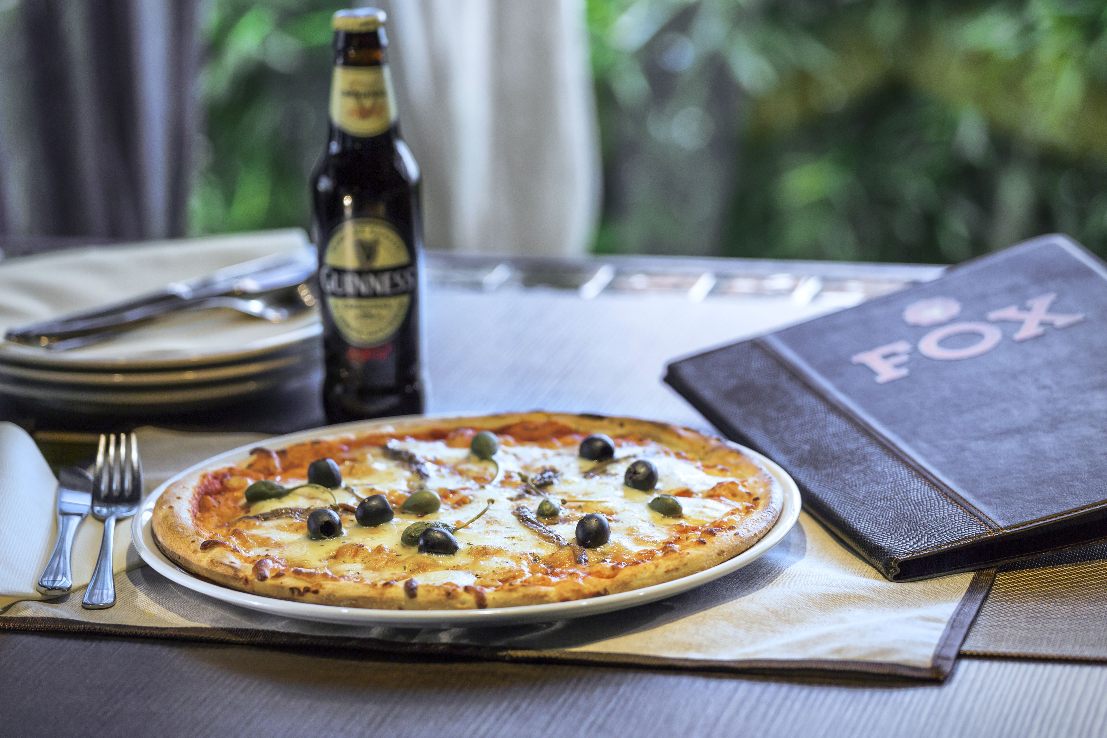 Eine Pizza auf einem Teller mit einer Bierflasche und einem Buch mit dem Titel "FOX" auf einem Tisch.