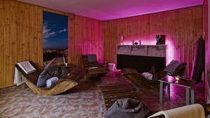 Habitación con paredes de madera, un ventanal y vista a la playa. Hay varias sillas de madera y una mesa con una lámpara.