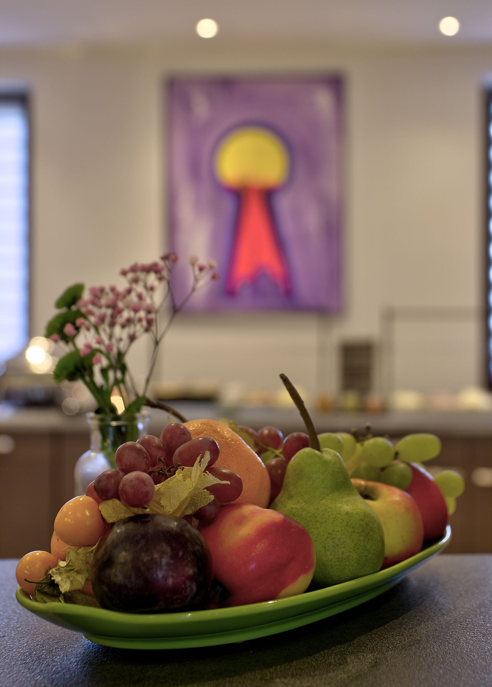 Eine Obstschale auf einem Tisch, im Hintergrund eine Blumenvase.