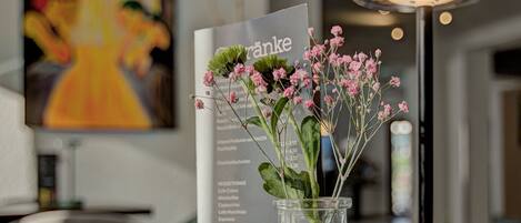 A clear glass vase with pink flowers on a wooden table, a menu, and a modern lamp.