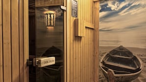 Un cuarto de sauna con una puerta de madera, un cartel que dice 'SAUNA REGELI' y vistas a un bote en la playa a través de la ventana.