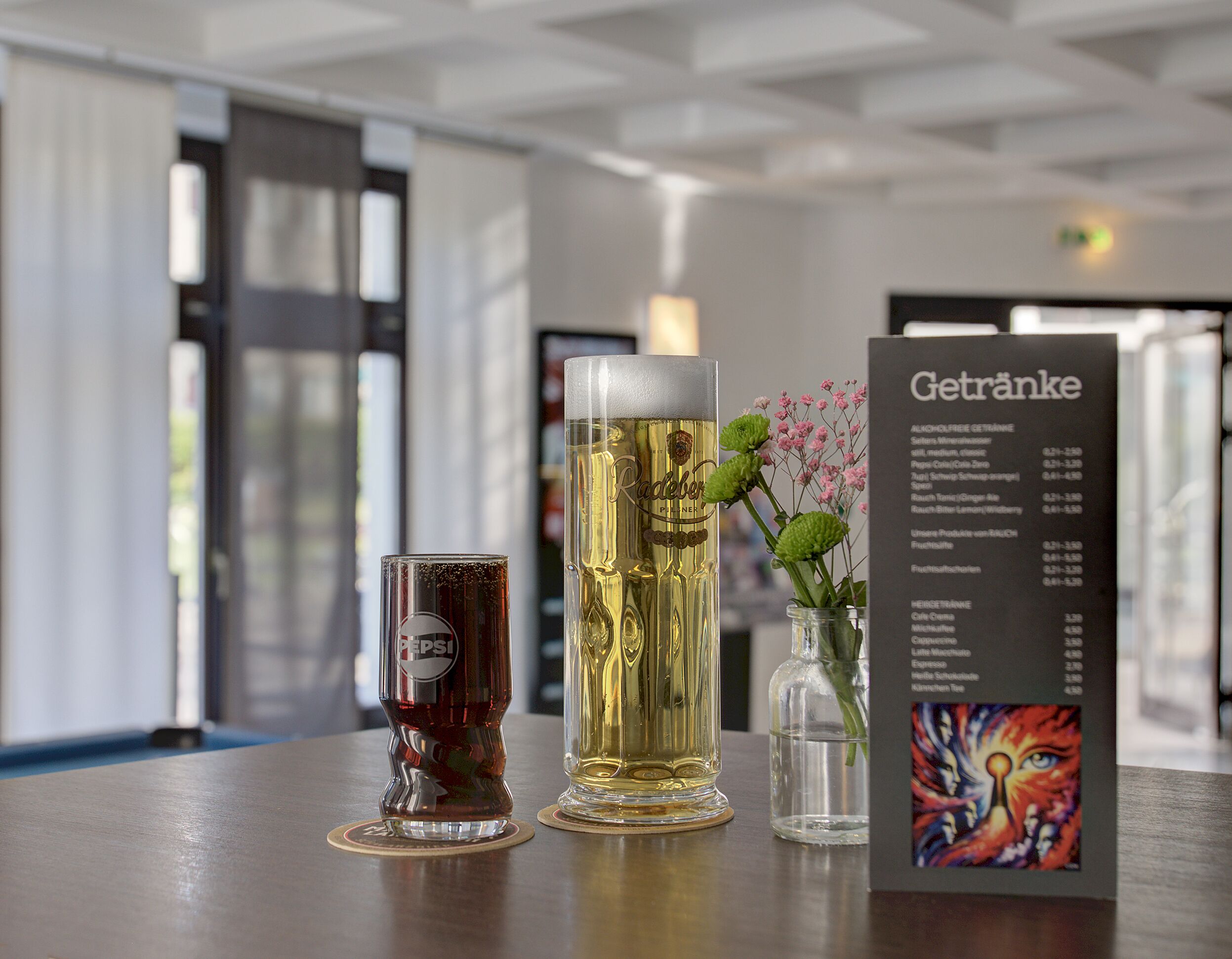Een tafel met een glas bier, een blikje Pepsi en een menukaart met de titel 'Getränke' met verschillende drankjes.