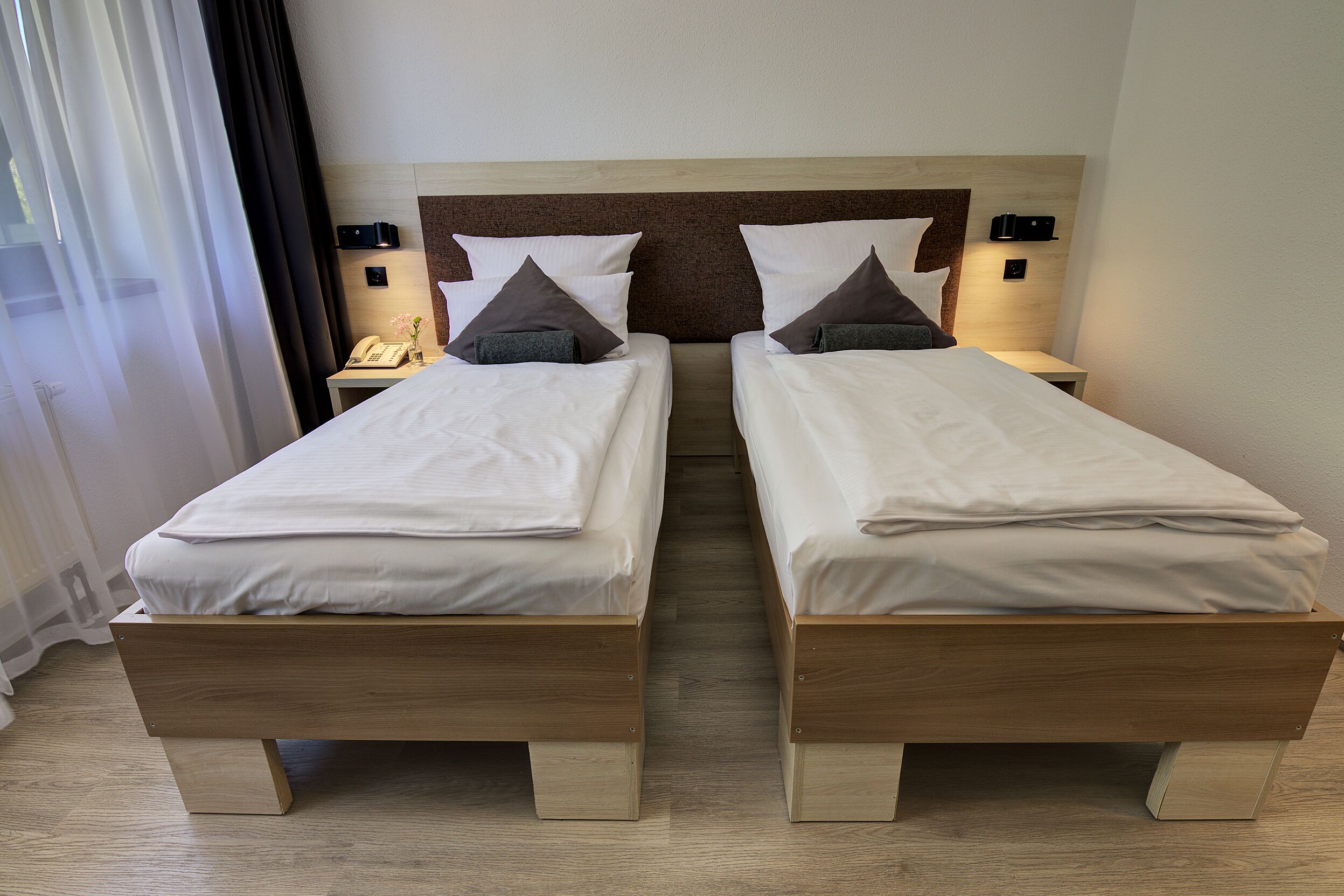 Un lit double avec une tête de lit en bois, deux tables de chevet avec des lampes et un rideau à la fenêtre.