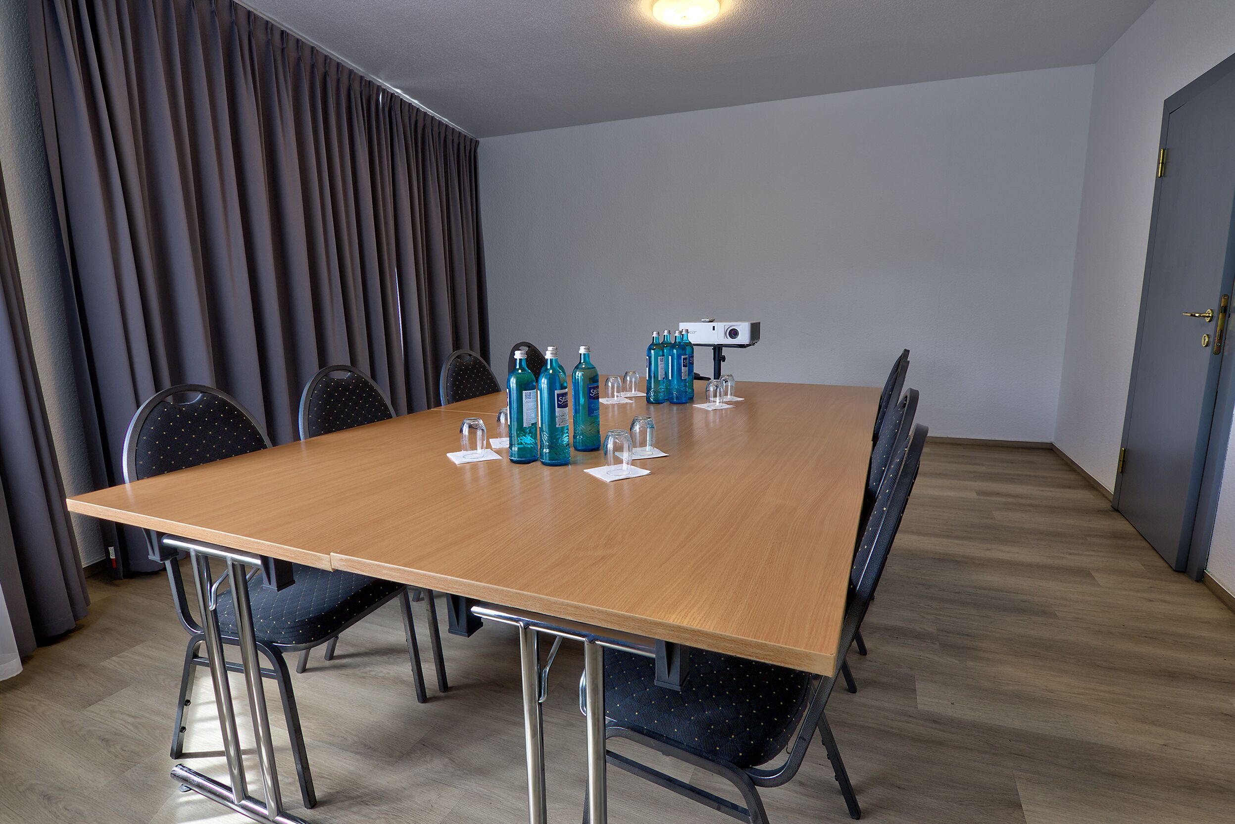 Ein Konferenzraum mit einem langen Tisch, sechs Stühlen und einem Projektor.