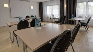 A conference room with a large table, chairs, a projector screen, and windows with curtains.