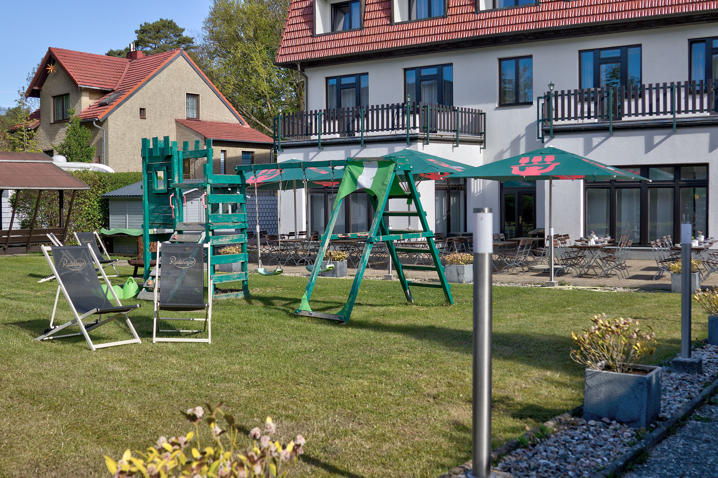 A playground with green equipment, outdoor seating, and a building with a red roof in the background.