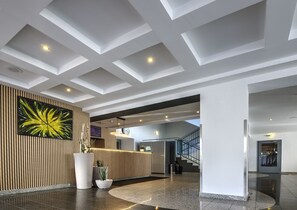 A modern lobby with a reception desk, a large abstract painting, a staircase, and a ceiling with recessed lighting. - Waldhotel Wandlitz (Wandlitz)