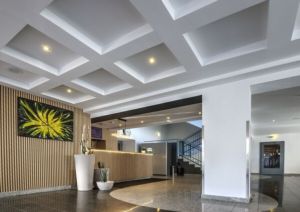 Um hall moderno com balcão de recepção, uma grande pintura abstrata, uma escadaria e um teto com iluminação embutida.