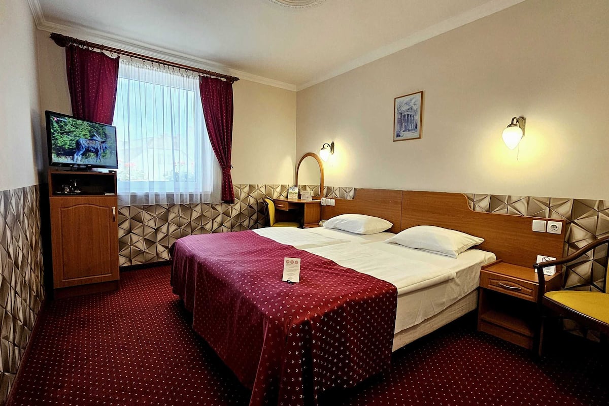 Ein Hotelzimmer mit Bett, Schreibtisch, Stuhl, Fernseher und einem fenster mit Vorhängen.