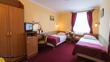 Habitación de hotel con dos camas individuales, un escritorio con ordenador, una silla, un armario y una ventana con cortinas.
