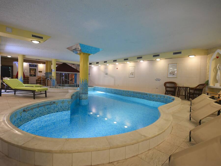 Une piscine intérieure avec un bord carrelé, des chaises longues et une statue.