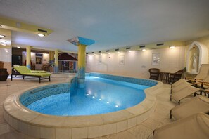 Une piscine intérieure avec un bord carrelé, des chaises longues et une statue.