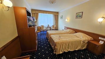 A hotel room with two beds, a desk with chairs, a television, and a window with curtains.