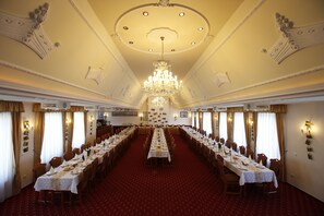 Une salle de banquet avec une longue table dressée pour un événement formel, un plafond décoré et des lustres.