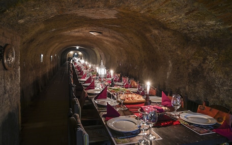 A long, dimly lit tunnel with tables set for a meal, featuring candles and dishes.
