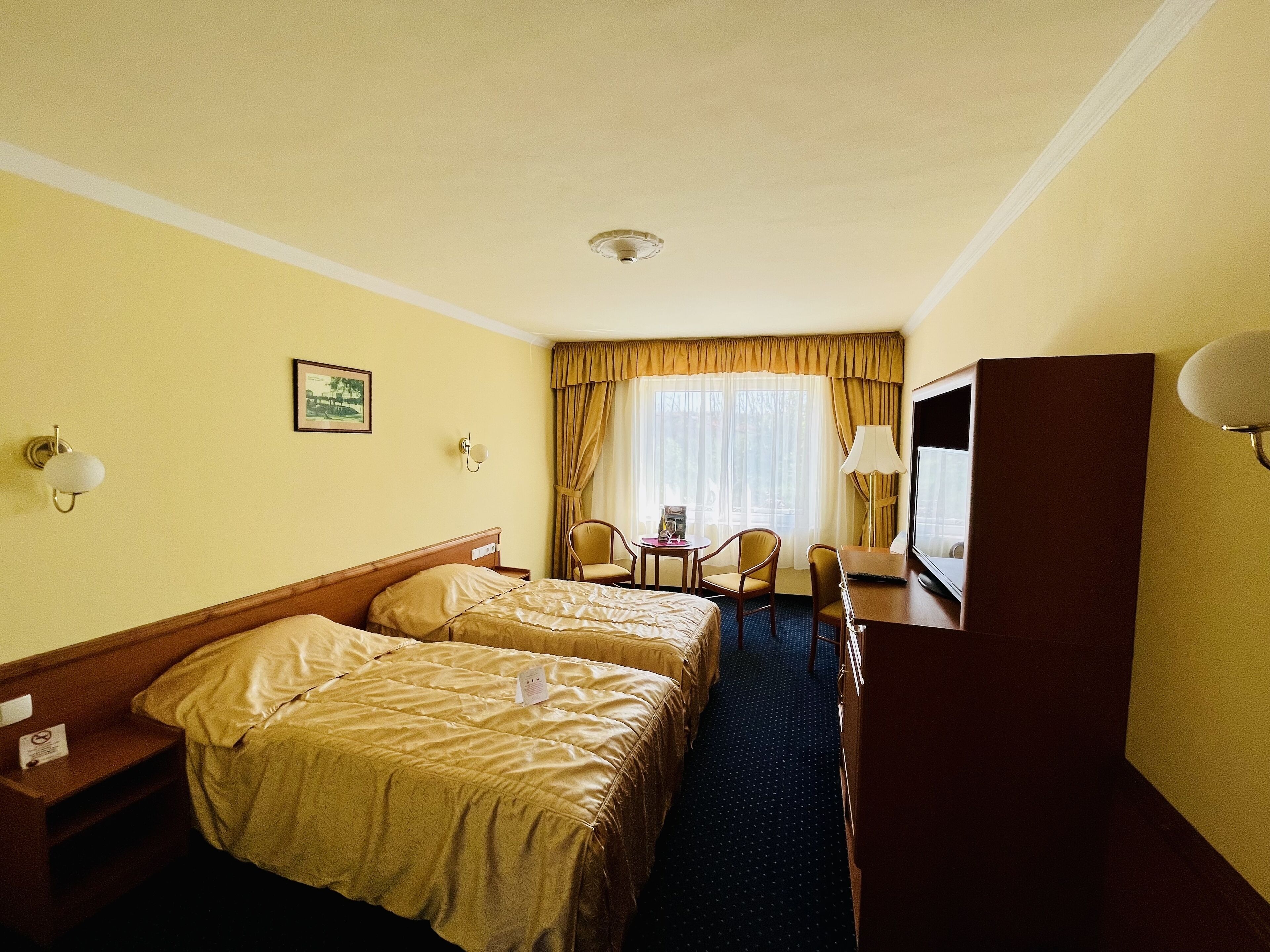 A hotel room with two beds, a desk, a chair, a television, and a window with curtains.