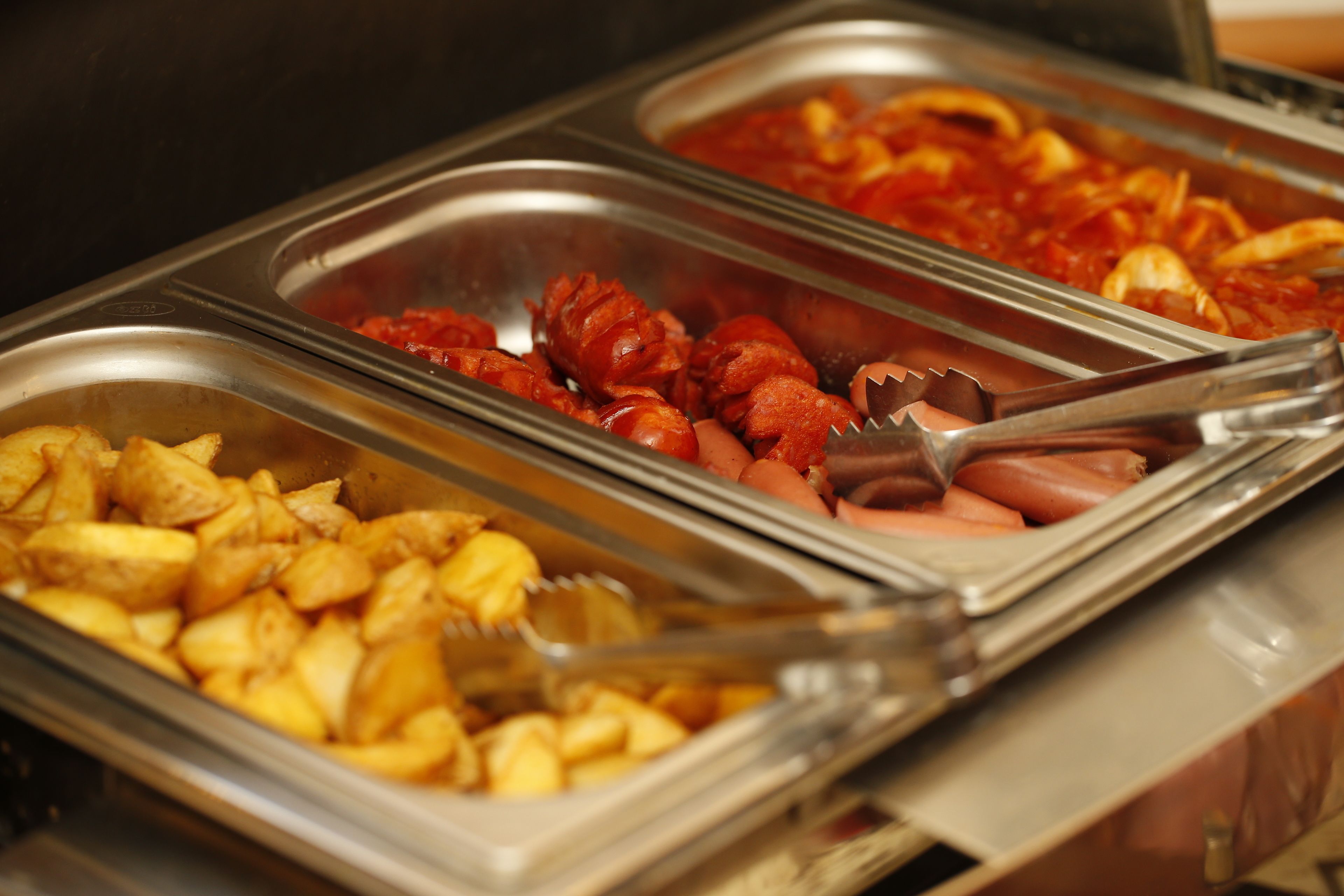 Een buffet met diverse gerechten, waaronder aardappelen, worstjes en een gerecht op tomatobasis.