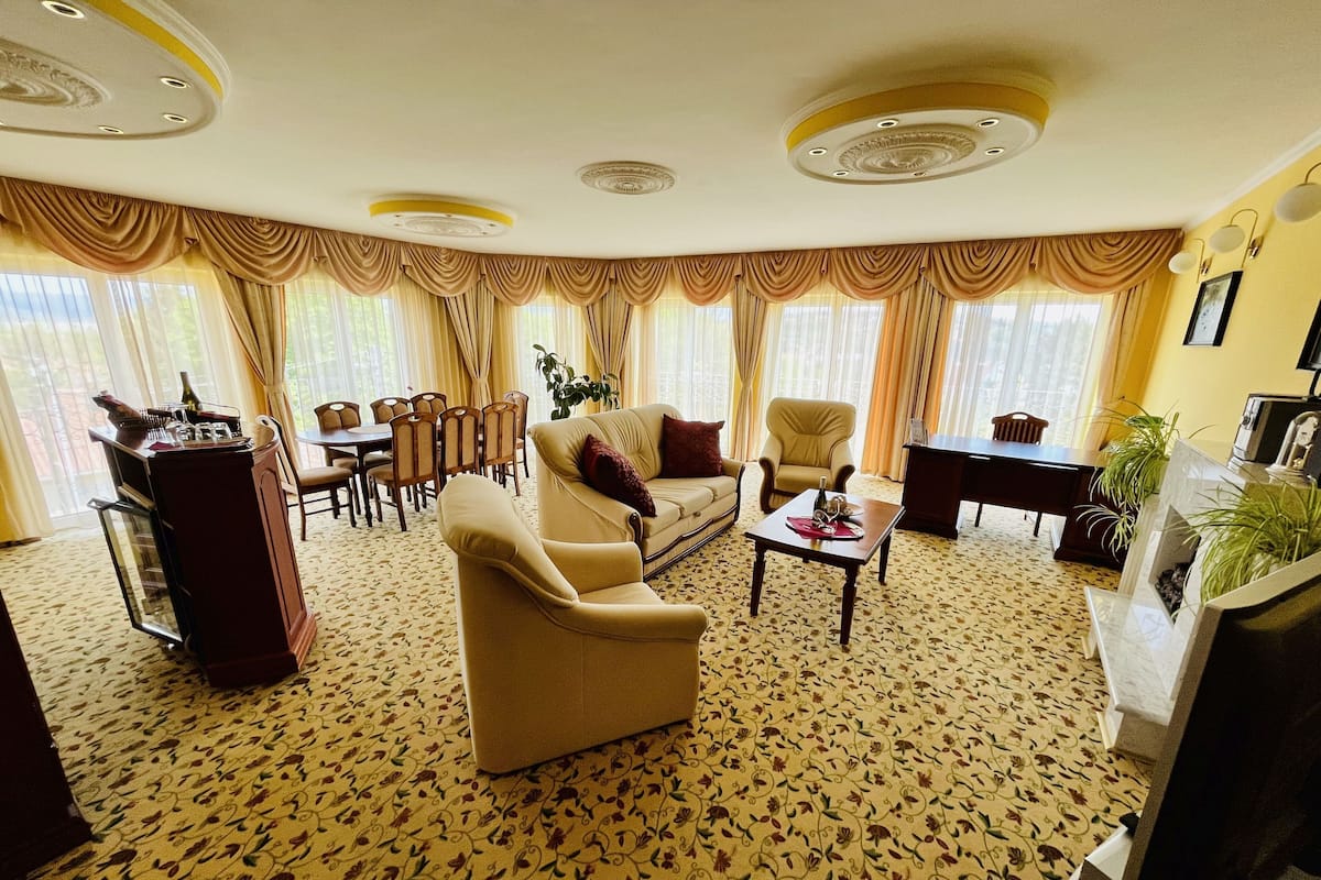 Ein geräumiges Wohnzimmer mit floralem Teppich, einem beigefarbenen Sofa, einem Couchtisch und einem Essbereich mit Stühlen und einem Tisch.