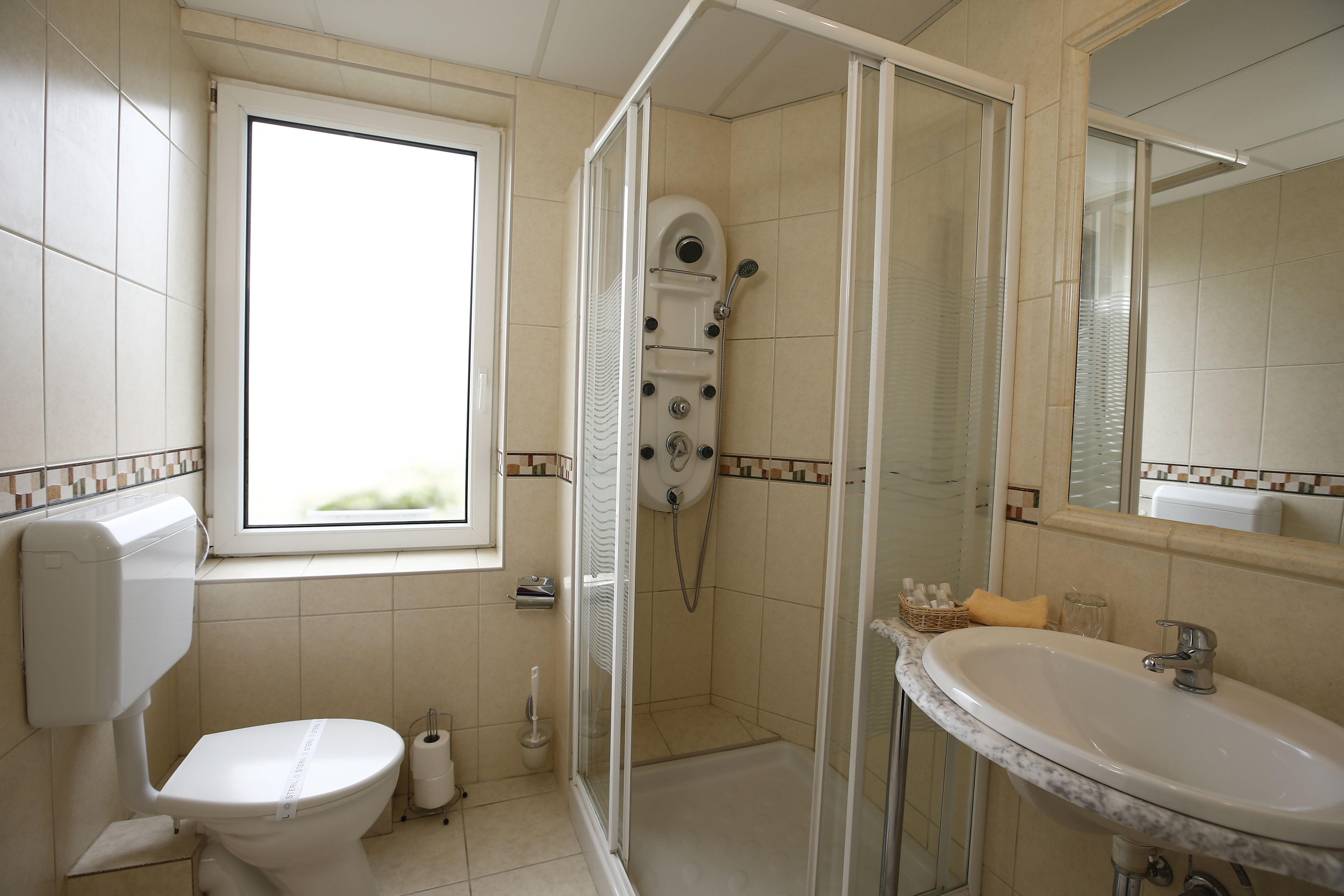 A bathroom with a toilet, a shower with a glass door, a sink, and a window.