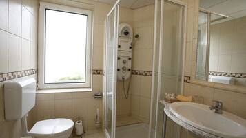 A bathroom with a toilet, a shower with a glass door, a sink, and a window.