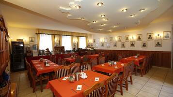Un espace repas avec plusieurs tables et chaises, une cuisine à l’arrière-plan et des œuvres d’art accrochées au mur.
