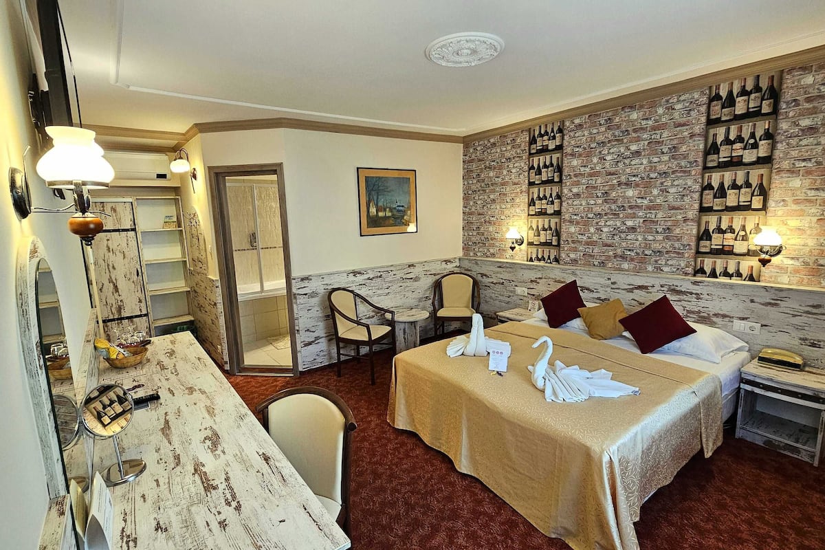 Ein Hotelzimmer mit einem Bett, zwei Sesseln, einem Tisch mit einer Lampe, einer Wand mit Weinflaschen und einer Tür zu einem Badezimmer.