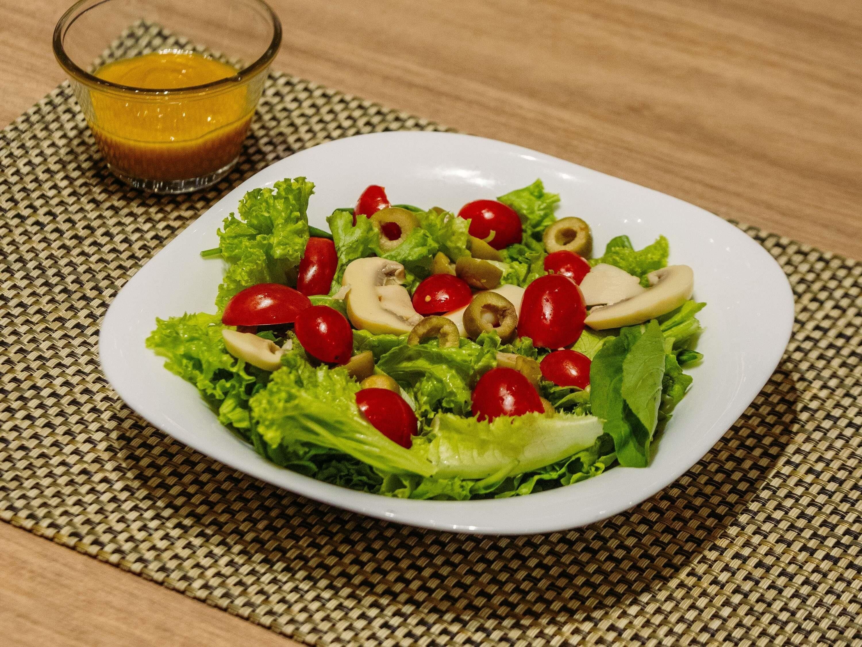 A plate of salad with lettuce, cherry tomatoes, and sliced mushrooms on a white plate.