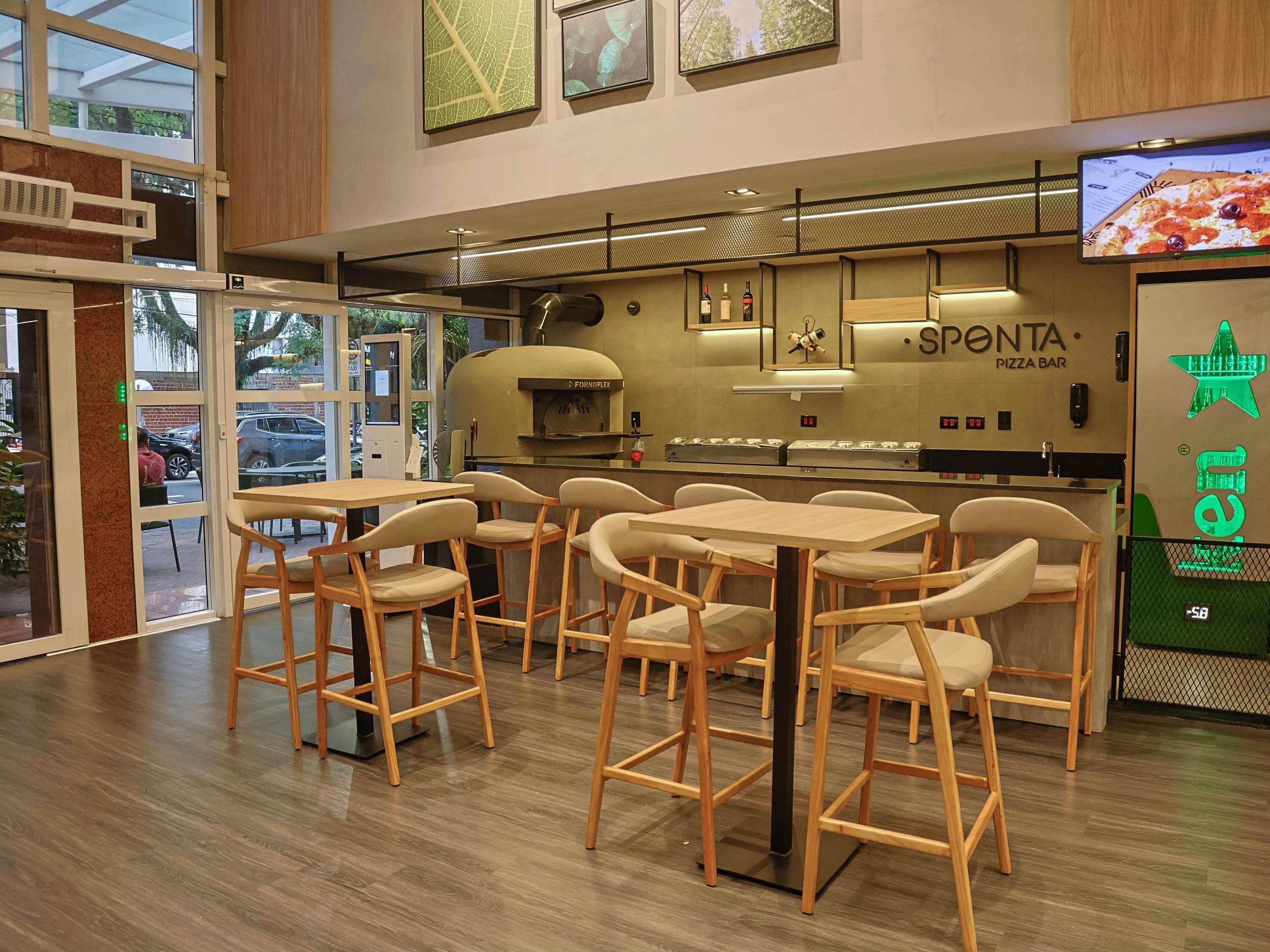 A pizza bar with a wood interior, tables, chairs, and a pizza display.