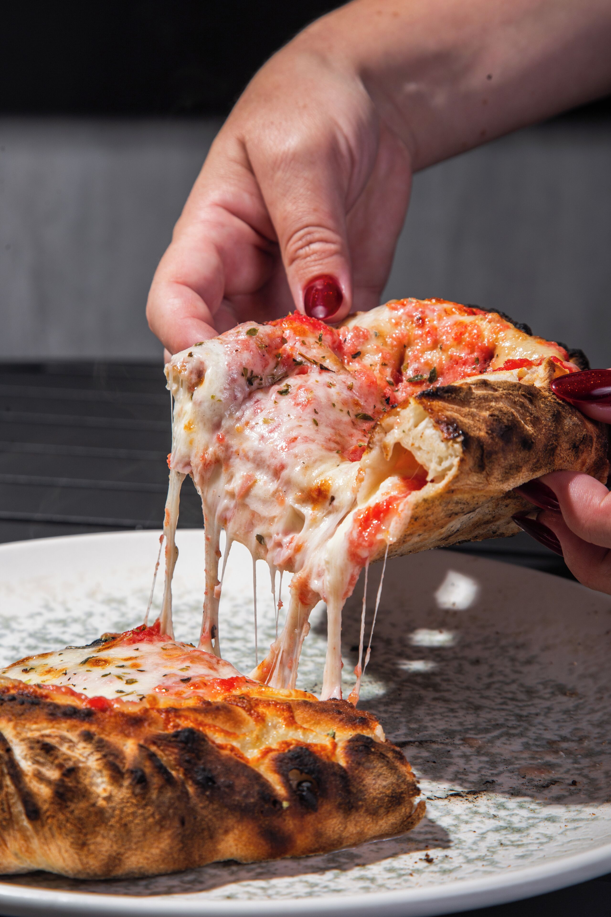 A hand holding a slice of pizza with melted cheese and tomato sauce, on a plate with a speckled design.