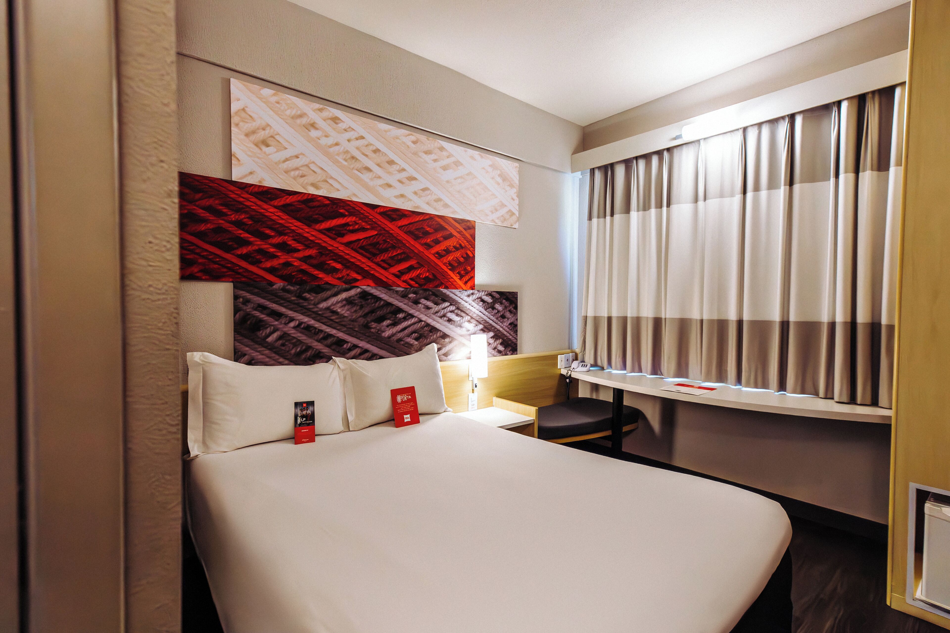 A hotel room with a bed, a desk, and a window with curtains.